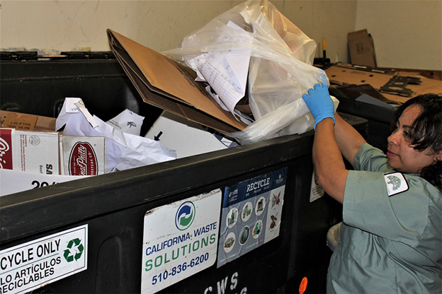 A woman putting a bag of papers and cardboard into a big recycling bin
